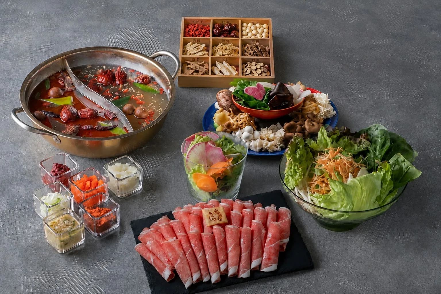 灰色の卓に麻辣湯と白湯の二色鍋、薬膳素材九種、きのこ盛り、鍋野菜、薬味六種、ロールラムを並べたコース全景