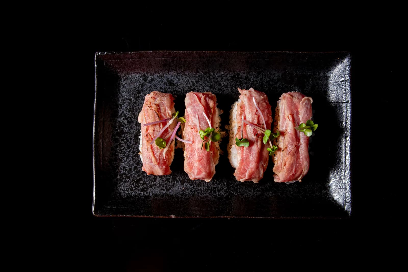 黒い角皿に炙りラム肉の握り寿司を四貫。刻みねぎを添え、黒背景に艶のある肉が浮かぶ