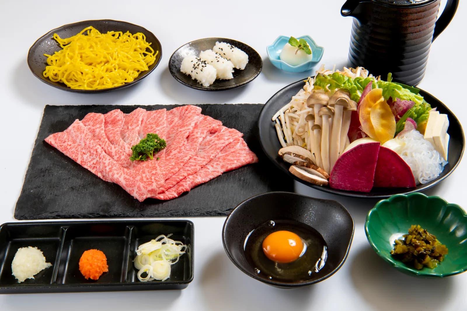 A full view of the course: marbled meat fanned out on black slate, arranged with mushrooms, vegetables, condiments and beaten egg