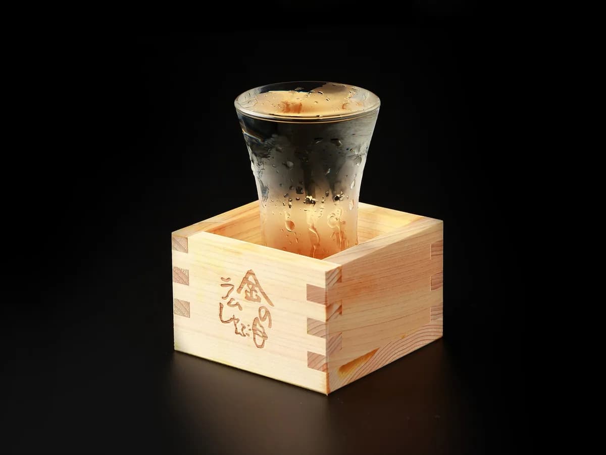 在带有金之目涮羊肉烙印的白木方杯中放入玻璃杯,斟满冰镇清酒。黑色背景下水珠闪光