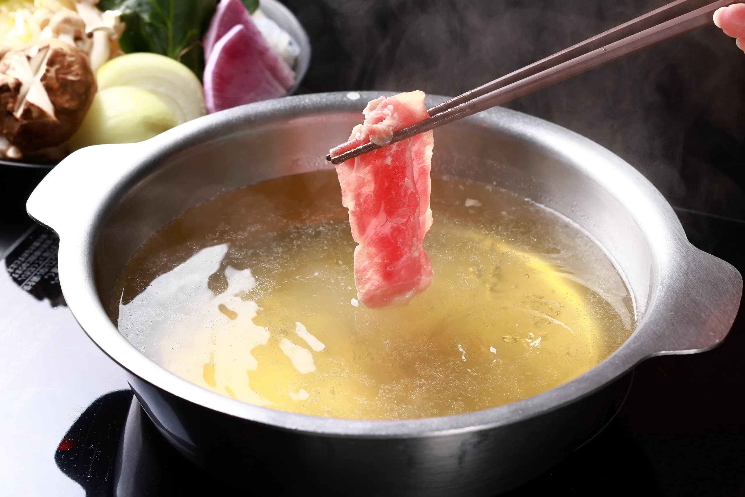A slice of Ginjo Lamb held with chopsticks and swished over the paitan pot; highland vegetables and shiitake sit behind