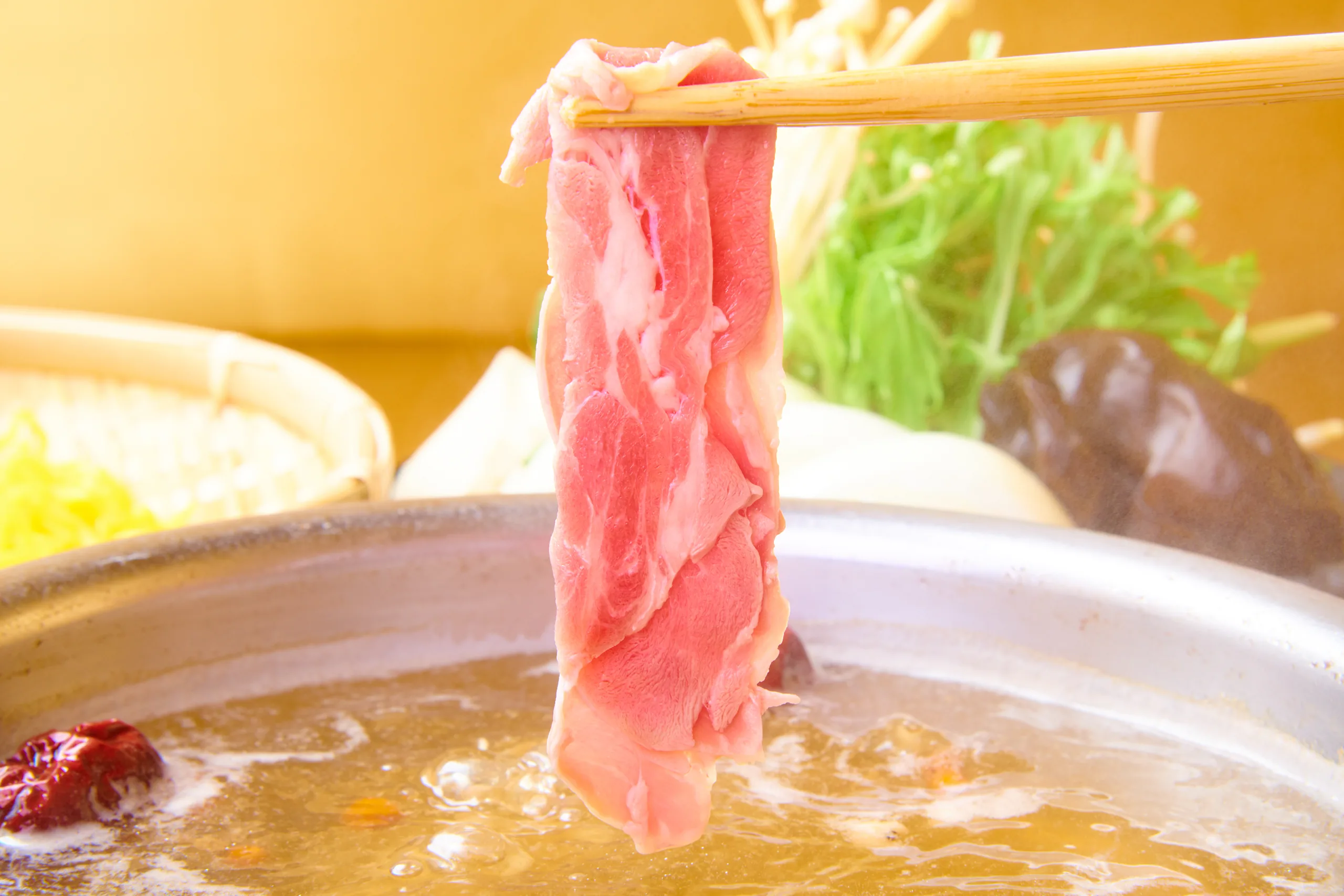 A thin slice of Ginjo Lamb lifted with chopsticks, wrapped in steam above the paitan pot; highland vegetables and shiitake sit behind