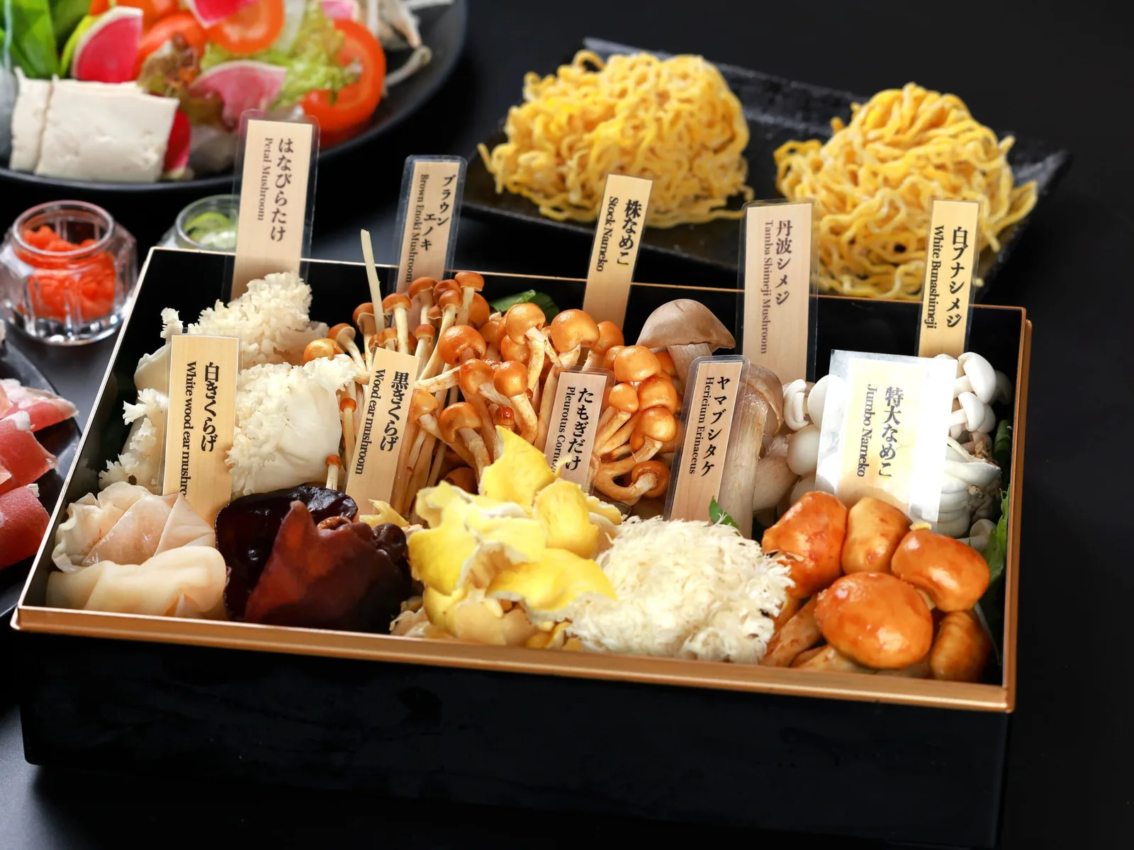 Ten kinds of mushrooms packed into a black lacquer box, with wooden tags in Japanese and English for Hanabiratake, Tamba shimeji, Yamabushitake and more