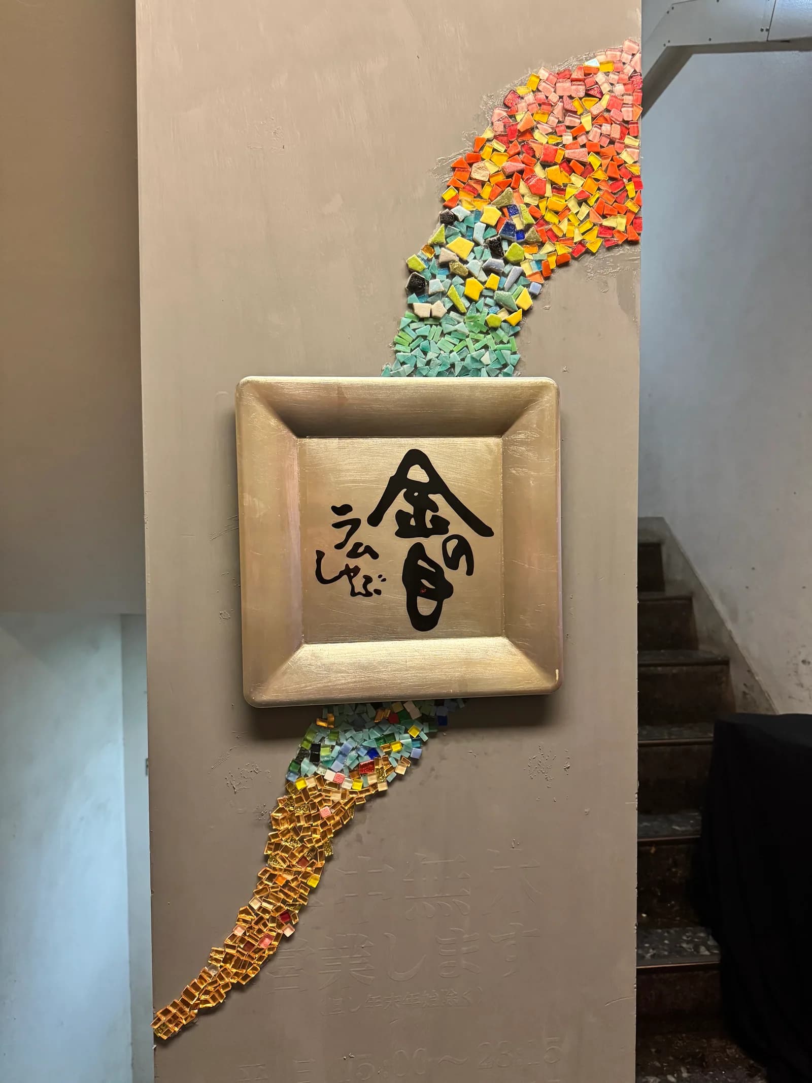 A wood-framed sign at the entrance of the Ginza Main Store; a mosaic of colored glass and gold leaf runs across the wall around the brushed KINNOME lettering