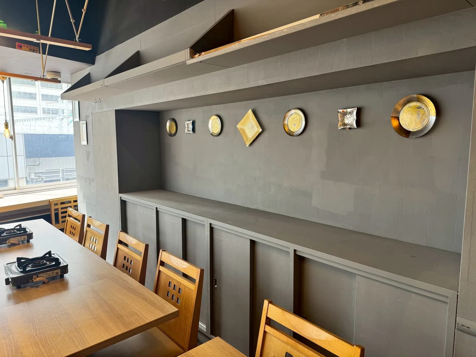 Table seating at the Ginza Main Store: gold and white decorative plates line a grey wall, and portable gas stoves are set into the wooden tables