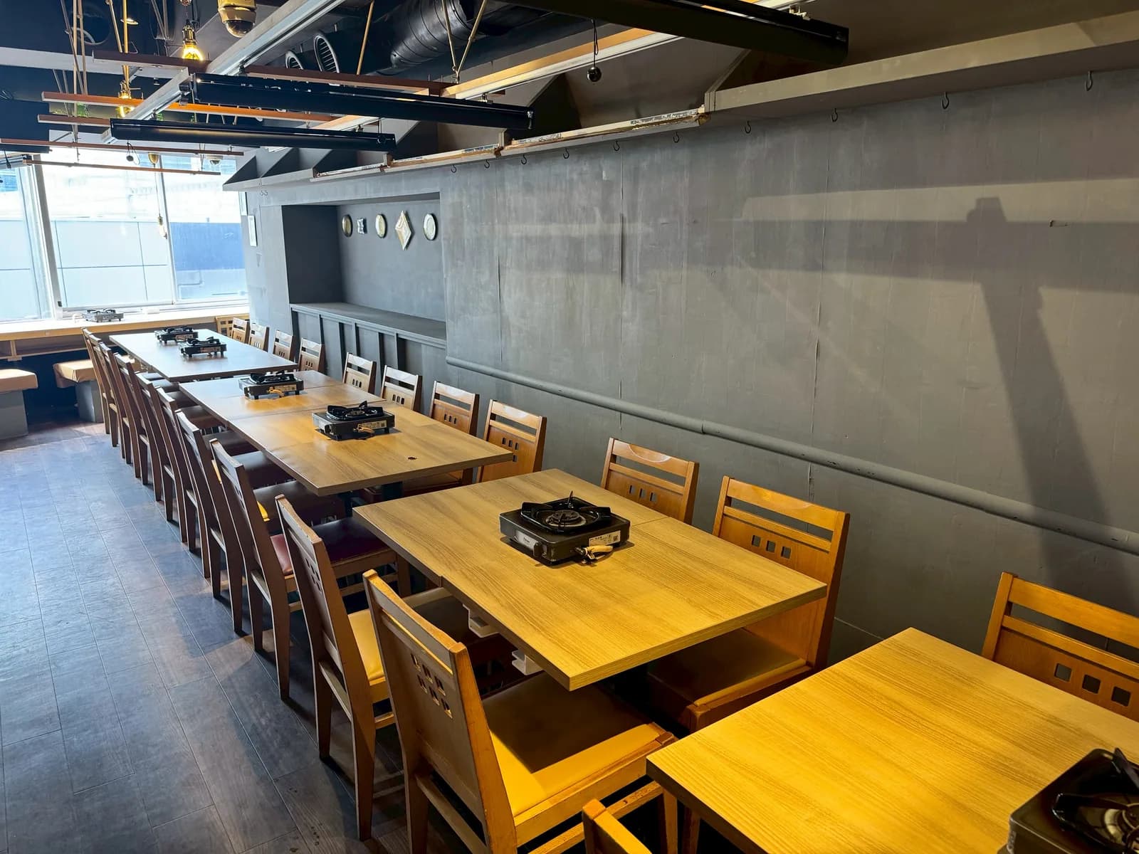 A full view of the Ginza Main Store interior: wooden tables fitted with portable gas stoves run in a single line to the window, with ducts exposed on the ceiling