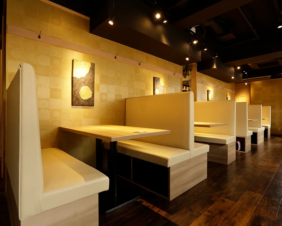 Booth seating at the Ikebukuro store: gold art panels hung at even intervals on a gold checkered wall, with cream bench seats and wooden tables