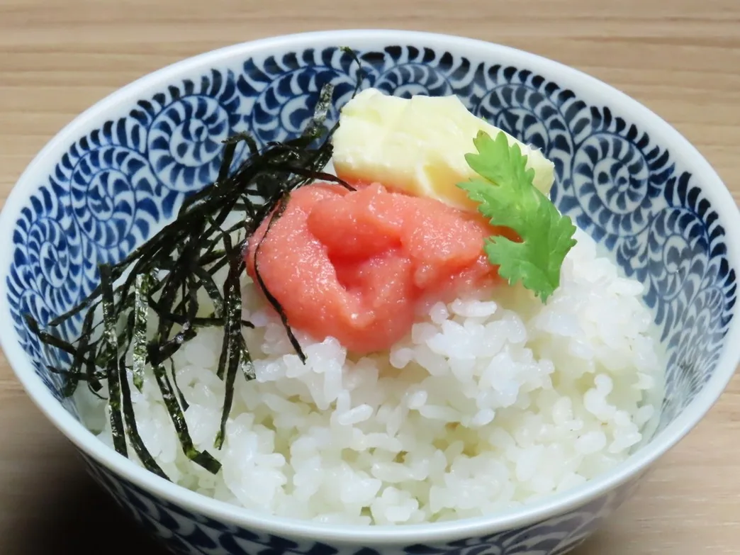Mentaiko rice to finish: white rice in an indigo Japanese-patterned bowl topped with mentaiko, shredded nori and butter, set on a wood-grain table