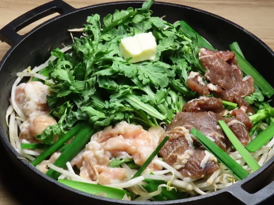 Lamb offal hot pot prepared in an iron pot before cooking: lamb offal, seasoned lamb, chrysanthemum greens and garlic chives arranged over bean sprouts, with butter at the center