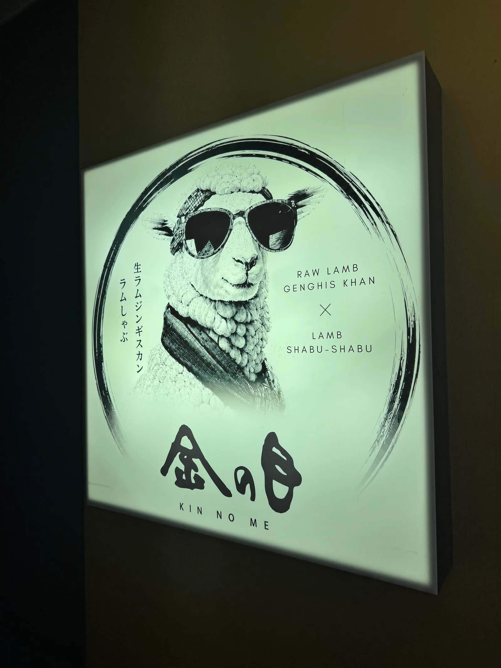 The round sign lit at the entrance of the Shibuya store, showing a sheep in sunglasses and the brushed KINNOME lettering