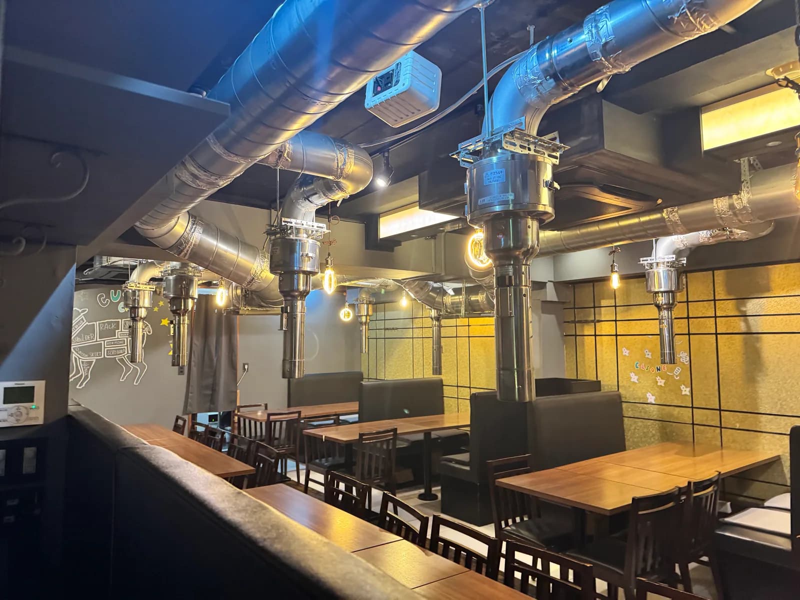 A view down the dining floor at the Shibuya store: wooden tables line a gold tile wall, with ceiling pipework and Edison bulbs running overhead