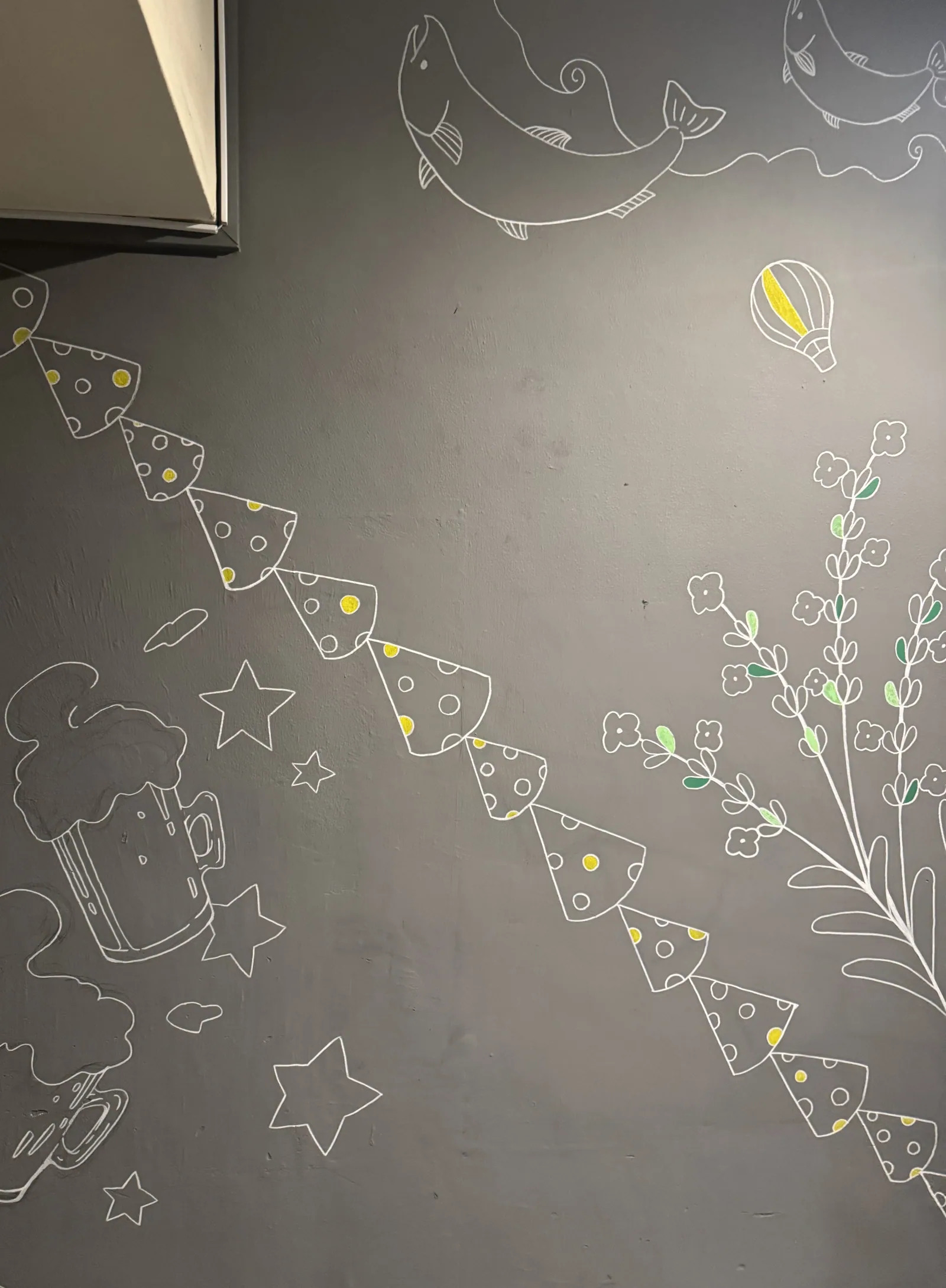 A mural drawn in white lines on a grey wall at the Shibuya store: polka-dot bunting runs diagonally, with fish, a hot-air balloon, a beer mug and flowering plants drawn in