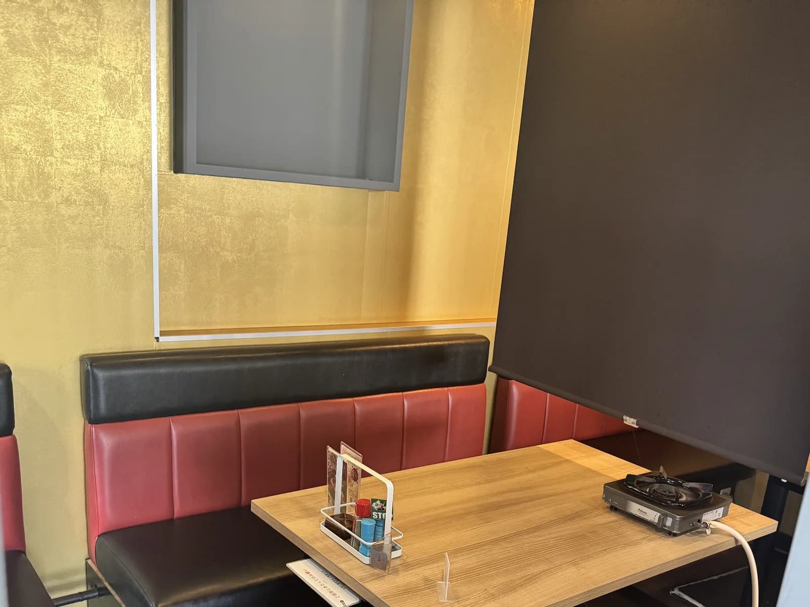 新宿店のボックス席。金箔調の壁を背に赤と黒のソファが木のテーブルを囲み、右手を黒いロールスクリーンで仕切る